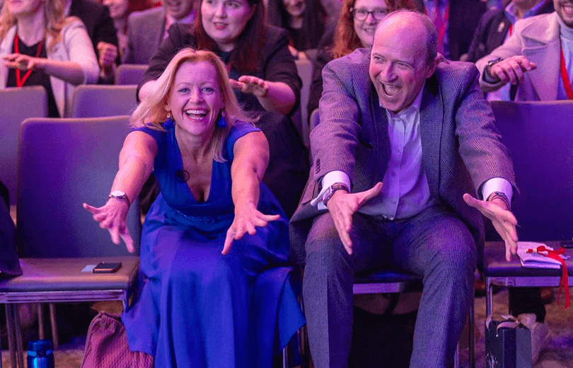 Man and woman laughing while stretching forward at a lively event.
