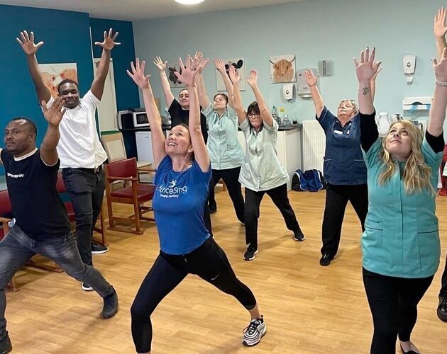 Group of people stretching upwards during a fitness session indoors.